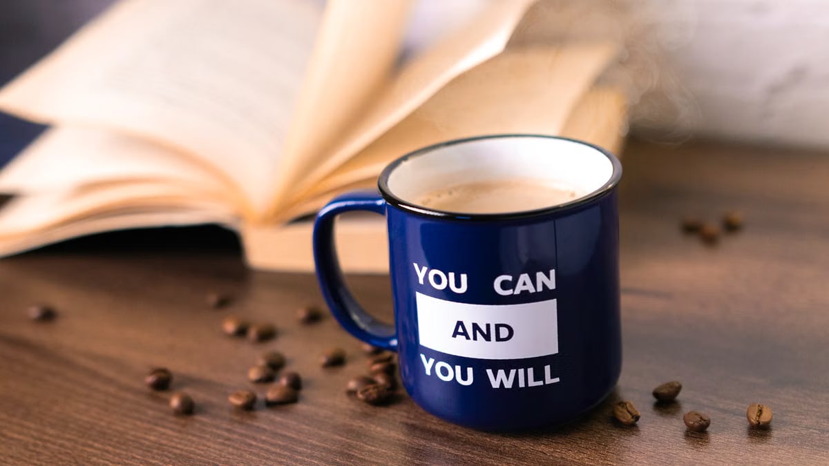 Inspirational coffee moment with a motivational quote on a mug beside an open book.